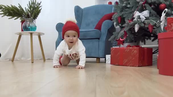 Lindo bebé en ropa de Navidad arrastrándose en el suelo de madera a su madre arrodillada con hermosos regalos — Vídeo de stock