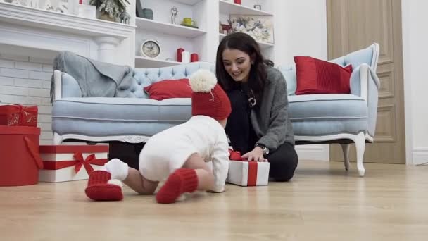 Doux bébé souriant rampant vers sa belle mère avec beaucoup de cadeaux de Noël qui sont assis près du canapé sur ses genoux — Video