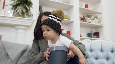 Sevimli küçük küçük kağıt kutu kemirme ve onun sevimli genç annesi güzel dekore edilmiş odada rahat kanepede onunla oturan