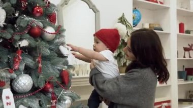 Dekore noel ağacı ve çocuk noel ağacı oyuncak almaya çalışırken yanında duran sevimli bebek ile yakışıklı gülümseyen anne