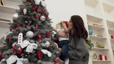Neşeli anne güzel dekore noel ağacı dokunmadan onu inanılmaz sevimli bebek tutmak