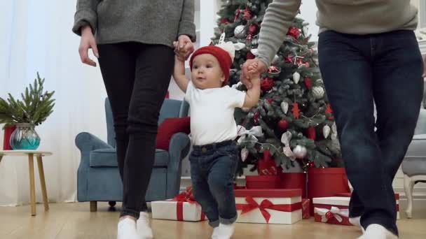 Atractiva imagen de la familia que toma de la mano a su dulce bebé y camina con él en la habitación decorada para celebrar la Navidad — Vídeos de Stock