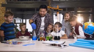 Laboratuvar sınıfında kimyasal sıvılar ve kuru buz kullanarak kimyasal deney yapan Asyalı öğretmen ile okul çocuklarının kimya grubu ders ön görünümü