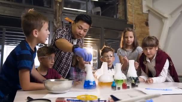 Asiatisk vetenskaps lärare driver ett experiment för sex skolbarn genom att sätta torris i fyra kolv med färgad vätska, det var reaktion av rök från torris i flaskor med vätska — Stockvideo