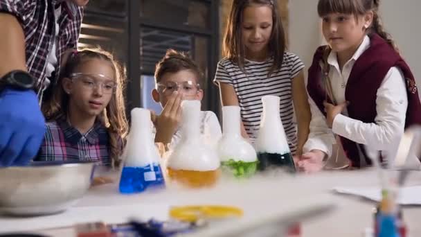 Asyalı fen öğretmeni altı okul çocukları için bir deney yapan ön görünümü renkli sıvı ile dört şişe içine kuru buz koyarak, sıvı ile şişelerde kuru buz duman reaksiyonu vardı — Stok video