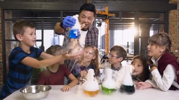 Jeune scientifique asiatique enseignant faisant des expériences avec de la glace carbonique pour les enfants en classe. Pendant l'expérience, enseignant tenant la fiole montrant la fumée de réaction et le liguide vert — Video