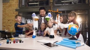 Ön görüş. Asyalı erkek fen öğretmeni, yoğun buharlaşmaya neden olan liguid ile iki şişe tutarak, chermical deney yapan genç öğrenciler öğretim