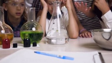 Kimya laboratuvarında kimyasal reaksiyonla çalışan bilim adamı genç öğrenciler ise reaksiyon sürecini izliyor. Laboratuvarda cam şişelerinde kimyasal deney sıvı yeşil renkler