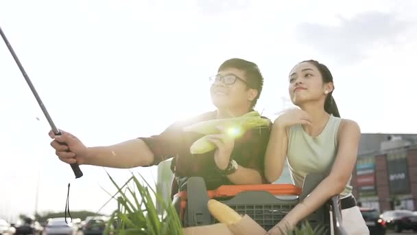 Красивий азіатський хлопець в окулярах тримає кукурудзу в руці і робить селфі зі своєю милою дівчиною біля магазину — стокове відео