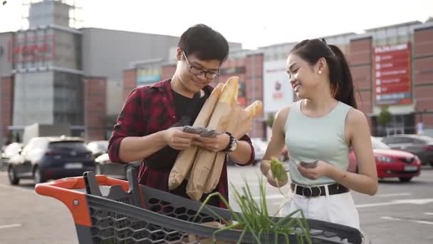 Jóképű fiatalember a szemüveg gazdaság Kenegessük a hosszú kenyér és a számlálás pénzt adott az ő aranyos mosolygó barátnője — Stock videók