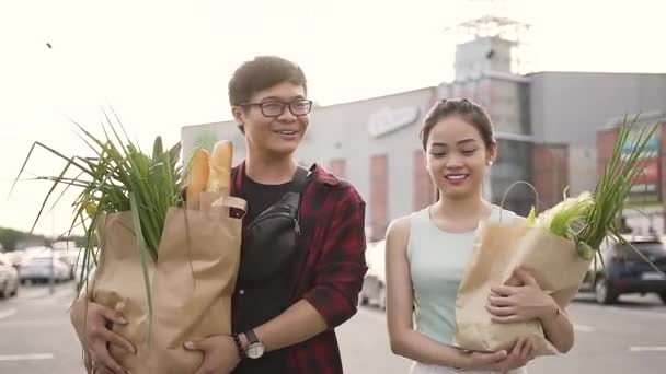 Atractivo alegre asiático hombre y mujer sosteniendo grandes bolsas de comida cerca del supermercado — Vídeo de stock