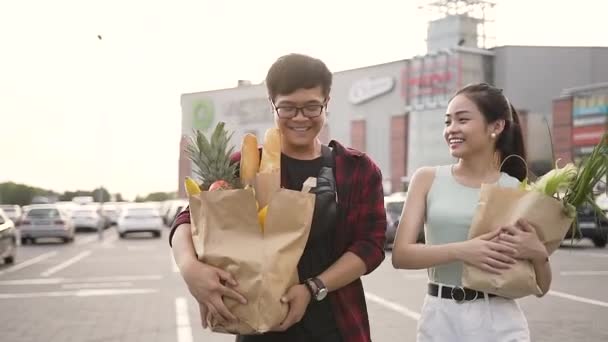 スーパーマーケットの近くに製品と彼らの手に大きな食品袋を運ぶ愛らしい幸せなベトナムのカップル — ストック動画
