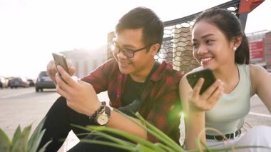 İyi görünümlü Asyalı gençler yiyecek ile kağıt torbayakınında yerde oturan ve telefonlarını kullanarak