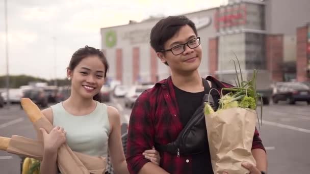 Красивая фотография улыбающихся счастливых вьетнамцев, стоящих с пакетами на фоне большого супермаркета — стоковое видео