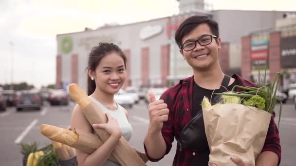 Happy glada vietnamesiska människor stående med matpåsar på bakgrunden av Big Store och visar OK — Stockvideo