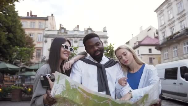 Grupo de jóvenes de razas mixtas guapos mirando el mapa para encontrar la ruta deseada, de pie cerca de hermosos edificios — Vídeo de stock