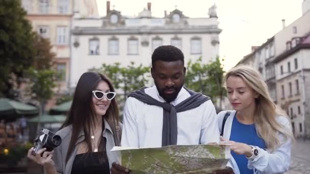 Pasangan ras campuran yang ceria berjalan di jalan kota dan melihat peta untuk melihat apakah mereka menuju ke arah yang benar — Stok Video