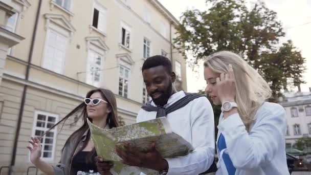 Gente joven feliz agradable que camina en la calle con arquitectura hermosa y que explora el mapa de la ciudad — Vídeo de stock