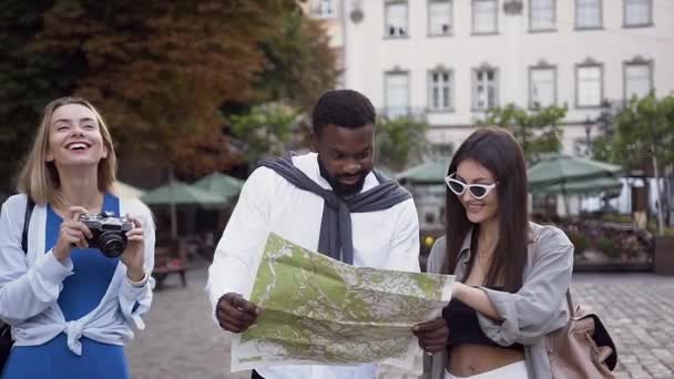 Gut aussehende lächelnde Frau fotografiert lupenreine Architektur, bis ihre gemischten Rassen Freunde auf der Touristenkarte suchen — Stockvideo