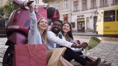 Serin scooter ve kadın arkadaş başlarının üzerinde eğlenceli bir şey gösteren yanında yerde oturan gülümseyen mutlu gençler