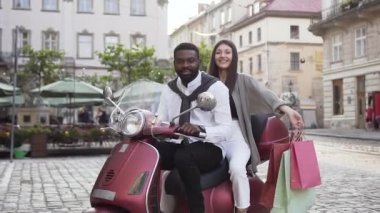 Sevimli neşeli karışık ırklar çift scooter ve kız elinde tutan oturan şehir mimarisinin arka planda alımları