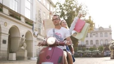 Çekici genç çift kentsel sokakta scooter sürme ve mutlu kadın alımları ile el kaldırdı