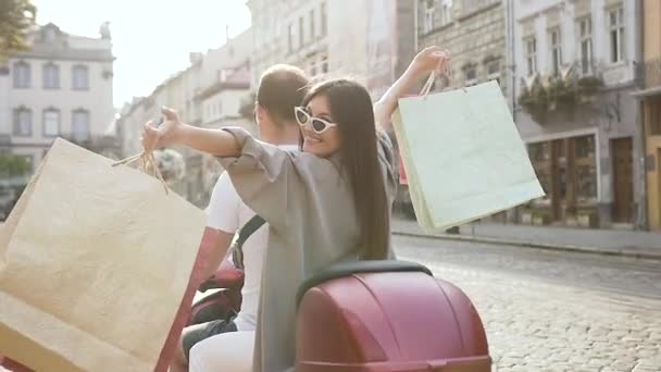 Atractiva imagen de la encantadora dama eufórica en gafas de sol de moda y compras montando en el hermoso scooter con su amigo a través de la calle urbana — Vídeo de stock