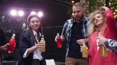 Birlikte eğlenen ve gün batımında alkolsüz içecek şişelerini birbirine bağlayan sevimli ince gençlik grubu