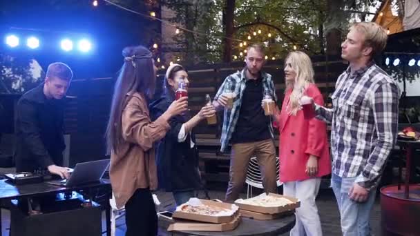 Dobře vypadající, příjemní mladí kamarádi, kteří dávají vysoké 5 lahví nealkoholických nápojů a odpočívají v altán s hudbou — Stock video