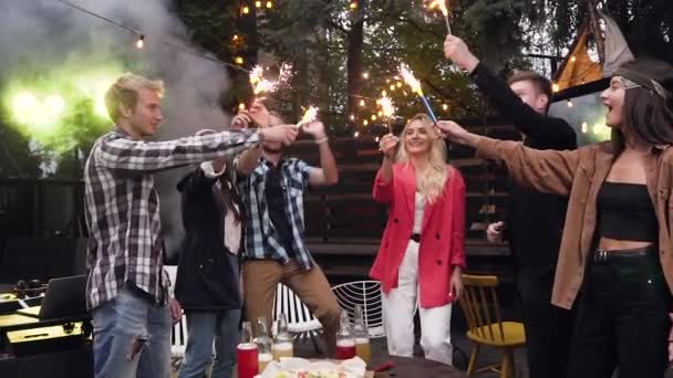 Cheerful good-looking young friends holding in their hands lighting sparklers and having fun together — Stock Video