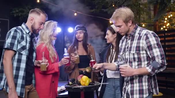 Härligt uppblåst unga människor stående nära grill med kokta grönsaker och spottar flaskor med alkoholfria drycker — Stockvideo