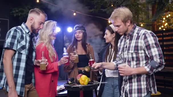 Encantadores jóvenes eufóricos de pie cerca de la parrilla con verduras cocidas y botellas tintineo con bebidas no alcohólicas — Vídeo de stock