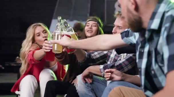 Συμμετοχή κομψών νεαρών συντρόφων που κάθονται στις καρέκλες και δίνουν ψηλά πέντε με μπουκάλια μη αλκοολούχων ποτών στο φιλόξενο κιόσκι — Αρχείο Βίντεο