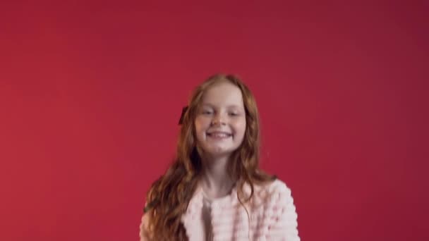 Nettes lächelndes Mädchen mit langen Haaren streut goldenes Konfetti auf roter Wand — Stockvideo