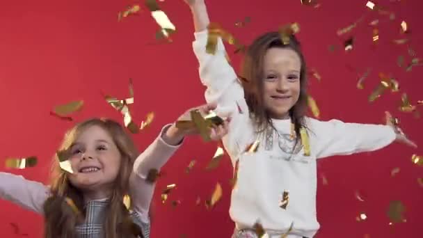Cámara lenta de las niñas bonitas lanzando confeti de oro sobre el fondo rojo — Vídeos de Stock