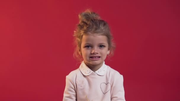 Крупный план очаровательной маленькой девочки с милой улыбкой разбрасывая конфетти на красном фоне — стоковое видео