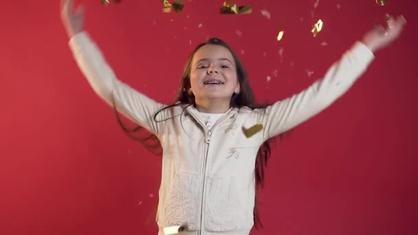 Gros plan de exubérante jeune fille joyeuse vêtue de vêtements élégants jetant des confettis sur le fond rouge — Video