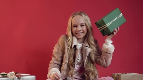 Αργή κίνηση του αξιολάτρευτο χαμόγελο έφηβος κορίτσι σε κομψά ρούχα κρατώντας στο χέρι της πράσινο κουτί με δώρο και κοιτάζοντας την κάμερα στο κόκκινο φόντο — Αρχείο Βίντεο