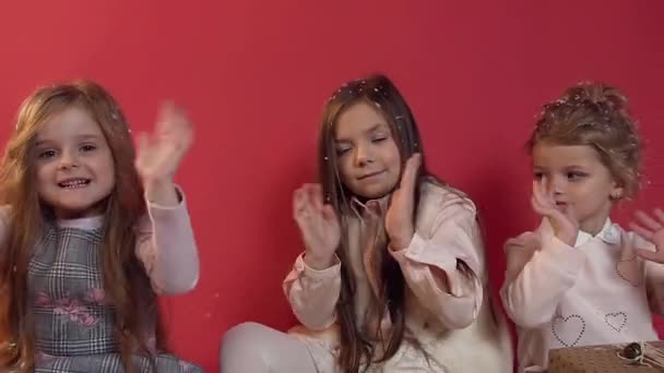 Underbar bild av tre vackra söta små flickor sitter på studion golvet bland vackert inslagna gåvor och vifta med händerna — Stockvideo