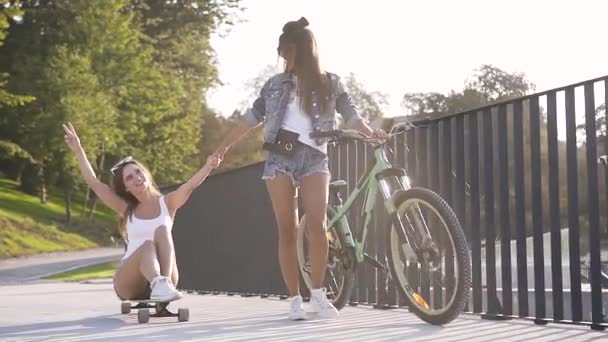 Mouvement lent de charmantes filles chaudes exubérantes avec vélo et planche à roulettes s'amusant ensemble dans la ruelle de la ville — Video