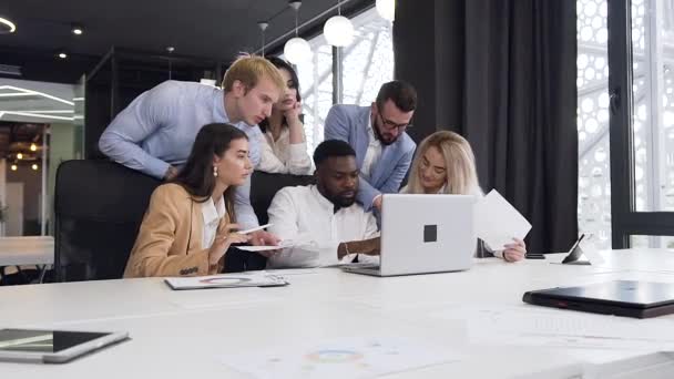 Lento movimento di giovani uomini d'affari fiduciosi di razze miste che lavorano sotto il loro progetto informatico congiunto al tavolo riunioni in ufficio — Video Stock