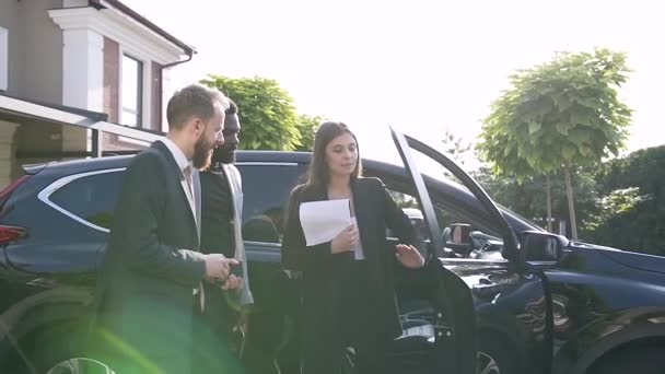 Professionell bilhandlare berättar om två intresserade affärsmän om hyra lyxig bil medan affärsmän tittar på auto och lyssna på återförsäljare om maskin översyn — Stockvideo