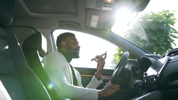 Vista lateral del hombre de negocios afroamericano guapo sentado en el coche de lujo mientras habla por teléfono con su socio de negocios — Vídeo de stock