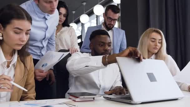 Hoge pittige dertiger jaren mixed races office managers werken samen in het kader van hun computer project aan de vergadertafel — Stockvideo