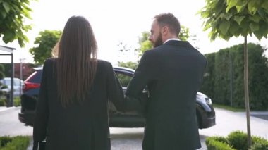 Siyah lüks araca doğru resmi giysiler içinde yürüyen başarılı, beyaz bir çiftin görüntüsü.