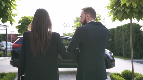 Widok z tyłu udanej młodej kaukaskiej pary w formalnych ubraniach spacerujących do czarnego luksusowego pojazdu — Wideo stockowe