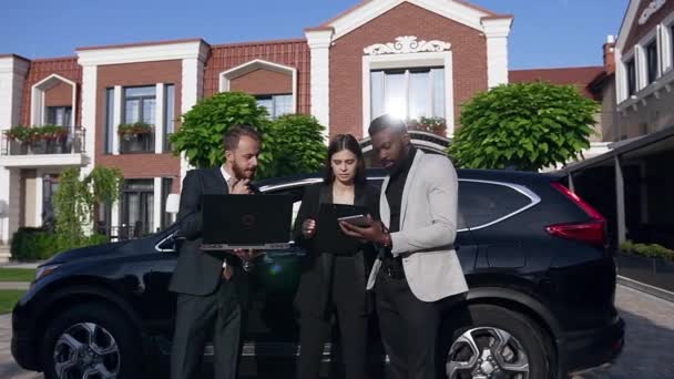 Fiatal üzletemberek formális öltözékben megvitassák az üzleti folyamatokat, miközben fekete autó és irodaház közelében állnak — Stock videók