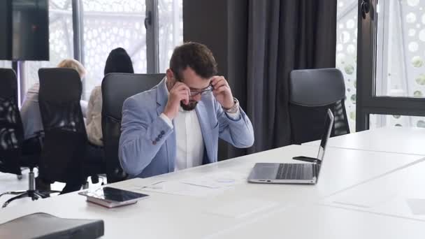 Vezměme si pohledný kancelářský manažer nosí brýle a pracuje na počítači a různé zprávy s grafy na svém pracovišti — Stock video