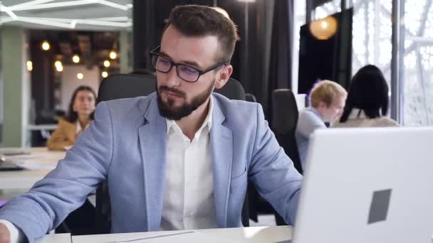 Mouvement lent de jeune homme d'affaires attrayant avec une barbe bien soignée et des lunettes assis sur son lieu de travail et montrant un panneau ok sur la caméra — Video