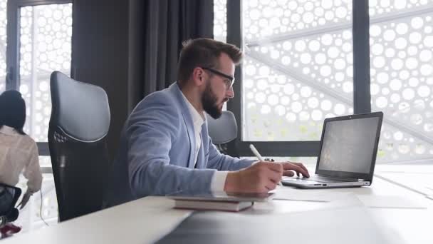 Portrait attrayant de jeune homme d'affaires barbu entreprenant qui travaille à l'ordinateur avec différents rapports, puis penché en arrière dans la chaise et est heureux du résultat à l'écran — Video